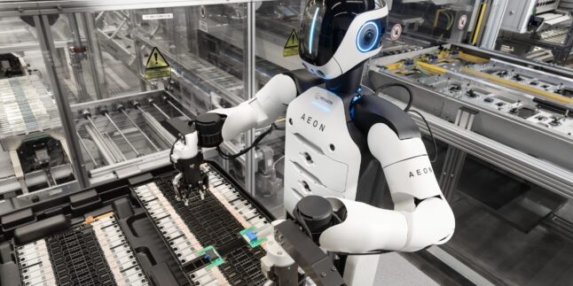 Ein humanoider Roboter mit weißer Brust und weißen Armen bei der Handhabung kleinerer Automobilkomponenten in einer automatisierten Anlage.