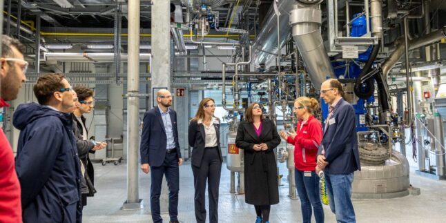 Besuchergruppe mit Schutzbrillen zwischen Industrieanlagen und Rohrleitungen im tesa-Werk Hamburg