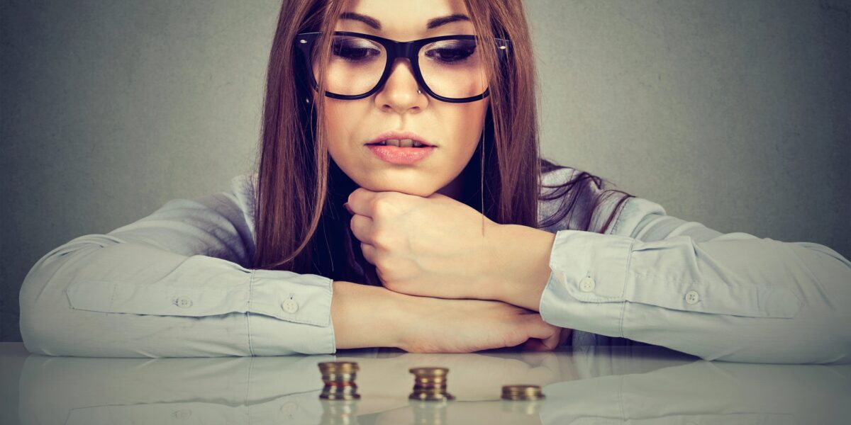 Junge, ehrgeizige Geschäftsfrau sitzt am Tisch und betrachtet einen wachsenden Stapel Münzen. Konzept: Finanzielle Freiheit, Zielerreichung, Erfolg.