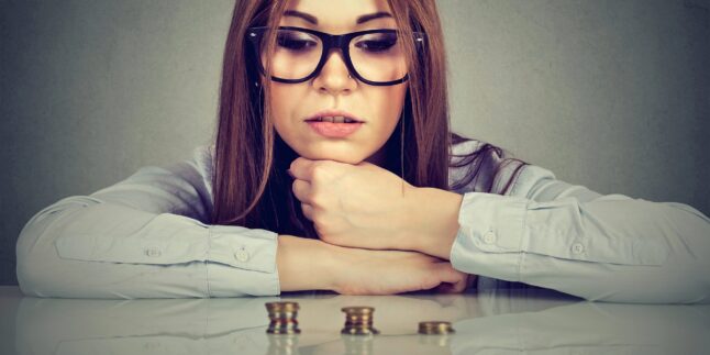 Junge, ehrgeizige Geschäftsfrau sitzt am Tisch und betrachtet einen wachsenden Stapel Münzen. Konzept: Finanzielle Freiheit, Zielerreichung, Erfolg.