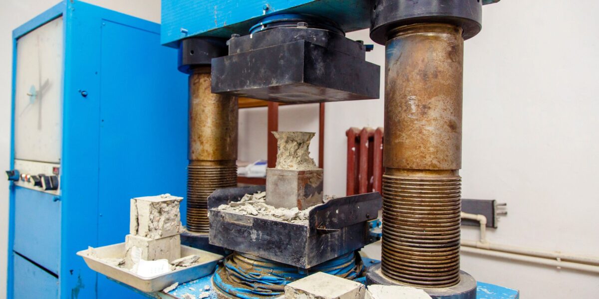 In einem Bau-Prüflabor wird ein kubischer Betonprobekörper in einer Druckprüfmaschine belastet
