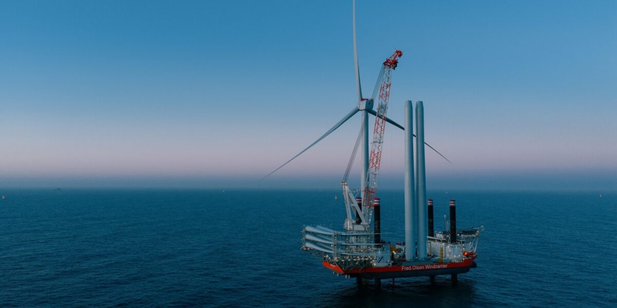 Errichterschiff auf offener See mit fast fertig errichteter Windkraftanlage in der Dämmerung.