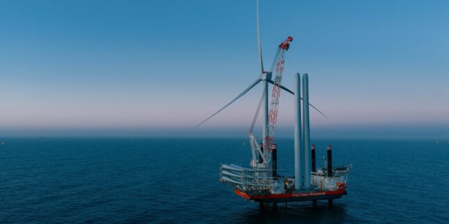 Errichterschiff auf offener See mit fast fertig errichteter Windkraftanlage in der Dämmerung.