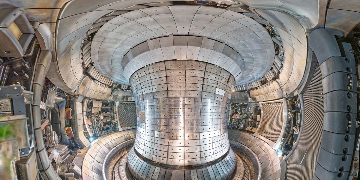 Blick in das Plasmagefäß des Fusionsexperiments ASDEX Upgrade in Garching. Die gesamte Innenwand ist mit metallisch glänzenden Wolfram-Ziegeln ausgekleidet, in der Mitte ragt die zentrale Säule des Tokamaks auf.