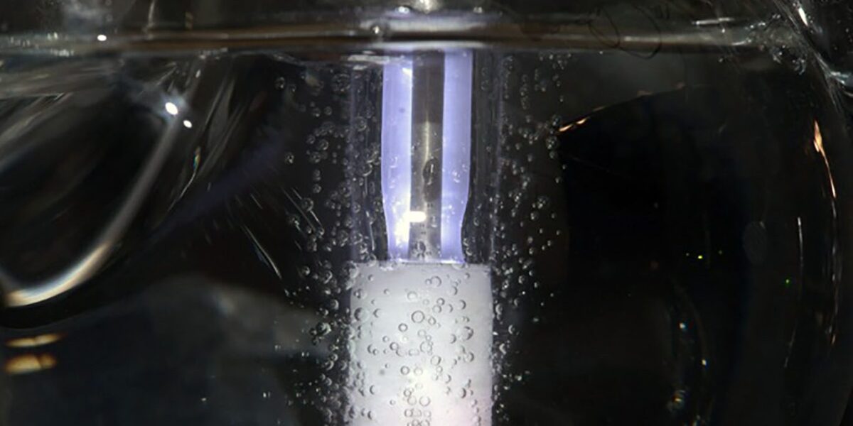 Glasrohr im Wasserbad mit einem weiß schimmernden Katalysator-Block und einem violett leuchtenden Plasmabereich