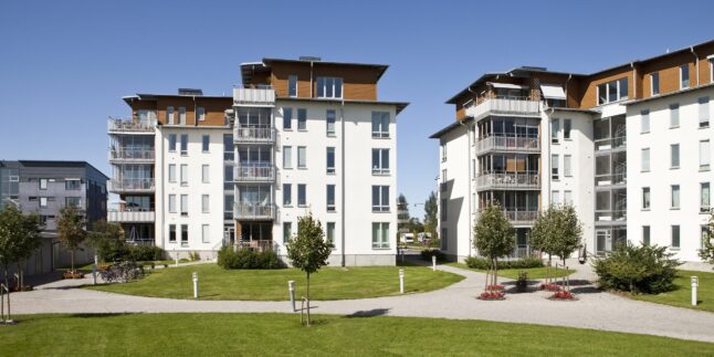 Zwei freistehende Mehrfamilienhäuser mit Rasen und Wegen davor.