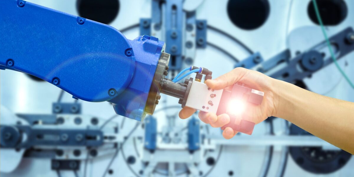 Ein Mensch fasst den Greifer eines Roboters an, wie beim Händedruck