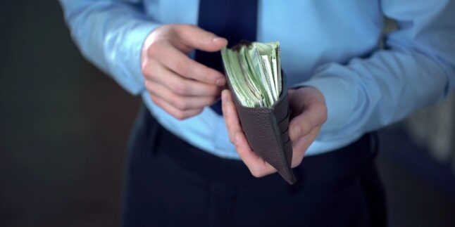 Bild eines wohlhabenden Geschäftsmanns, der ein geöffnetes Lederportemonnaie voller Dollarbanknoten hält, Finanzen