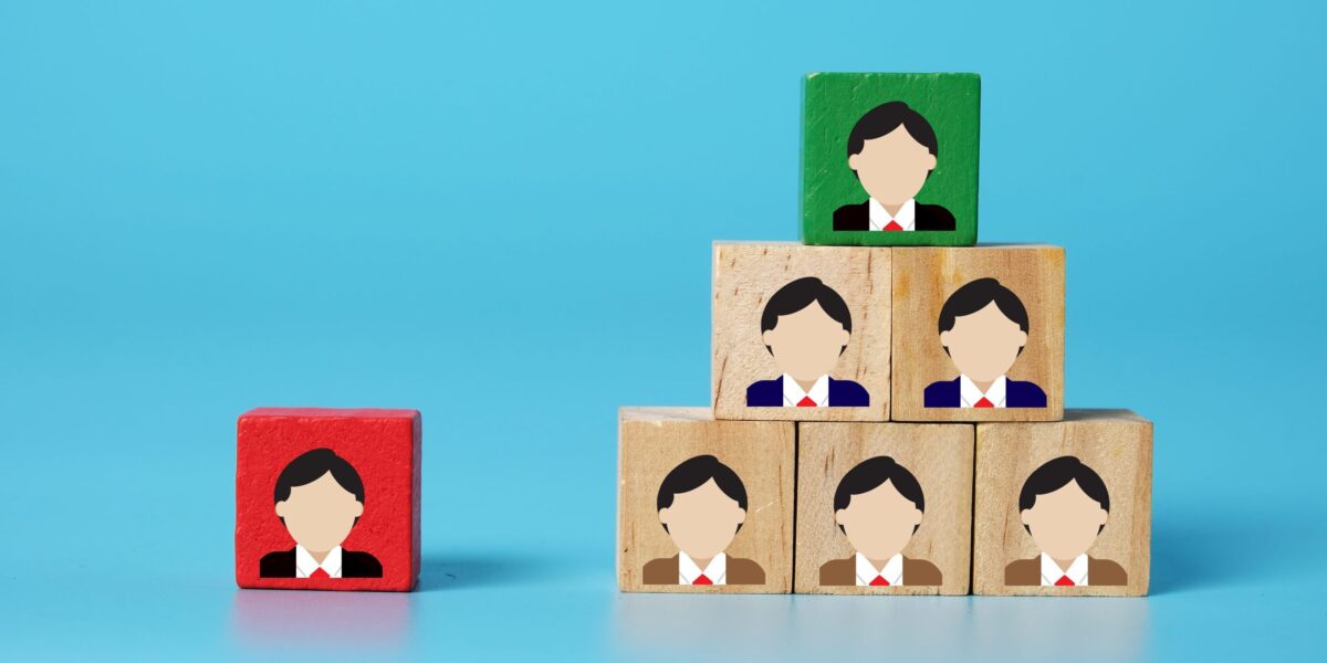 Symbolbild Führungskraft: Ein Bild von Holzklötzen mit Profil-Illustrationen. Unterschiedliche Hierarchieebenen sind durch verschiedene Farben gekennzeichnet. Konzept für Change Management und Organisation.