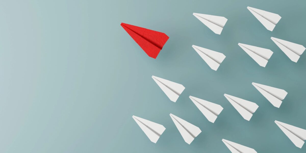 Viele weiße Papierflieger und rein roter Flieger als Gewinner