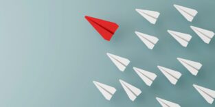 Viele weiße Papierflieger und rein roter Flieger als Gewinner