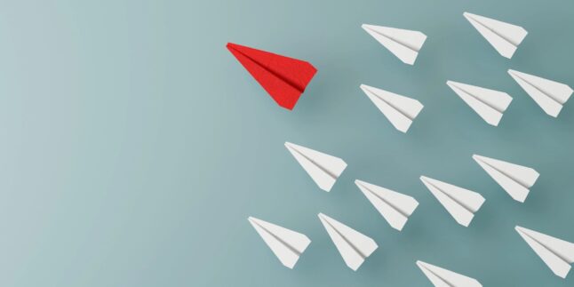 Viele weiße Papierflieger und rein roter Flieger als Gewinner