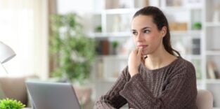 Eine Frau überlegt und sitzt am Computer.