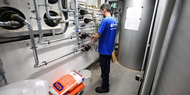 Ein Heizungsbauer installiert im Keller eines Mehrfamilienhauses die Technik für eine Wärmepumpe