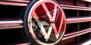 Eine Fahne der IG Metall spiegelt sich in einem VW Logo.