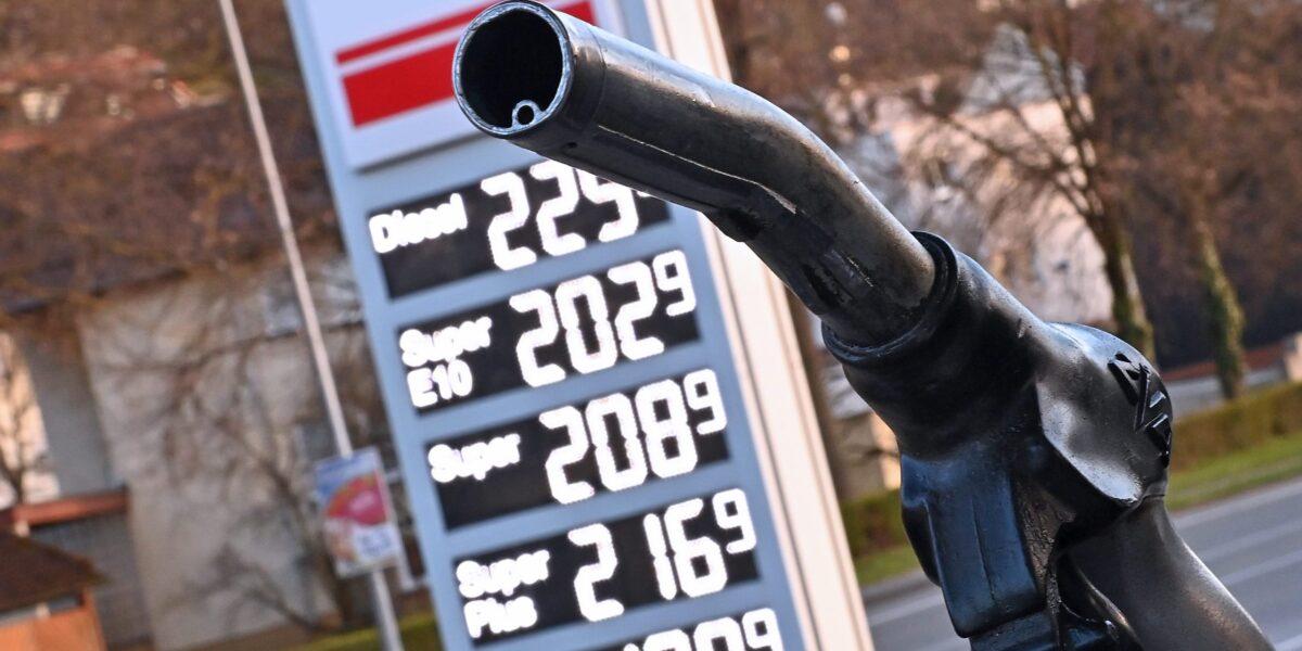 Tankrüssel vor der Spritpreisanzeige einer Tankstelle (verschwommen im Hintergrund)
