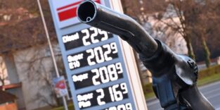 Tankrüssel vor der Spritpreisanzeige einer Tankstelle (verschwommen im Hintergrund)