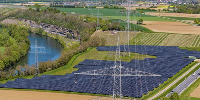 Luftaufnahme Stromtrasse vor Solarpark in Flußaue