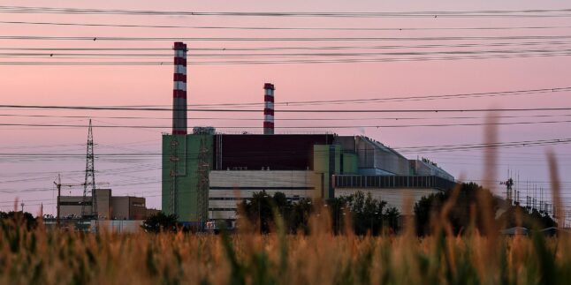 Ungarisches Atomkraftwerk Paks, im Vordergrund ein Feld am Himmel viele Stromleitungen