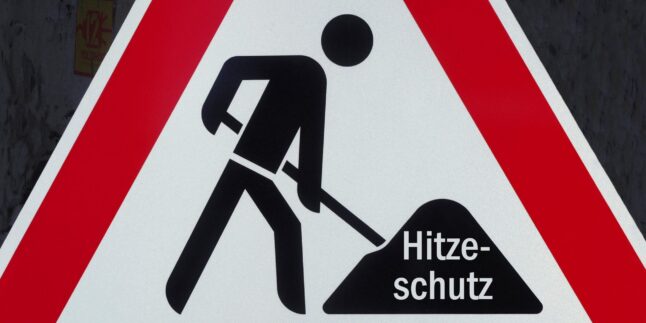 Baustellenverkehrsschild, hineinmontiert in den symbolischen Erdhaufen ist der Schriftzug "Hitzeschutz"