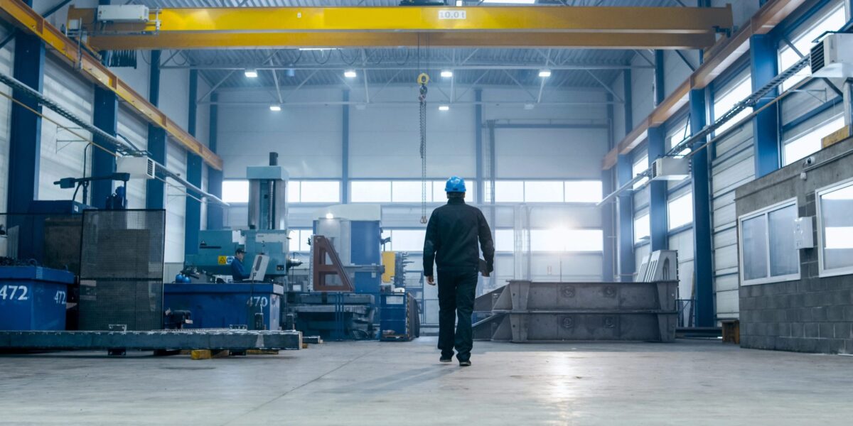 Ein Fabrikarbeiter mit Schutzhelm geht durch Industrieanlagen.