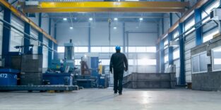 Ein Fabrikarbeiter mit Schutzhelm geht durch Industrieanlagen.
