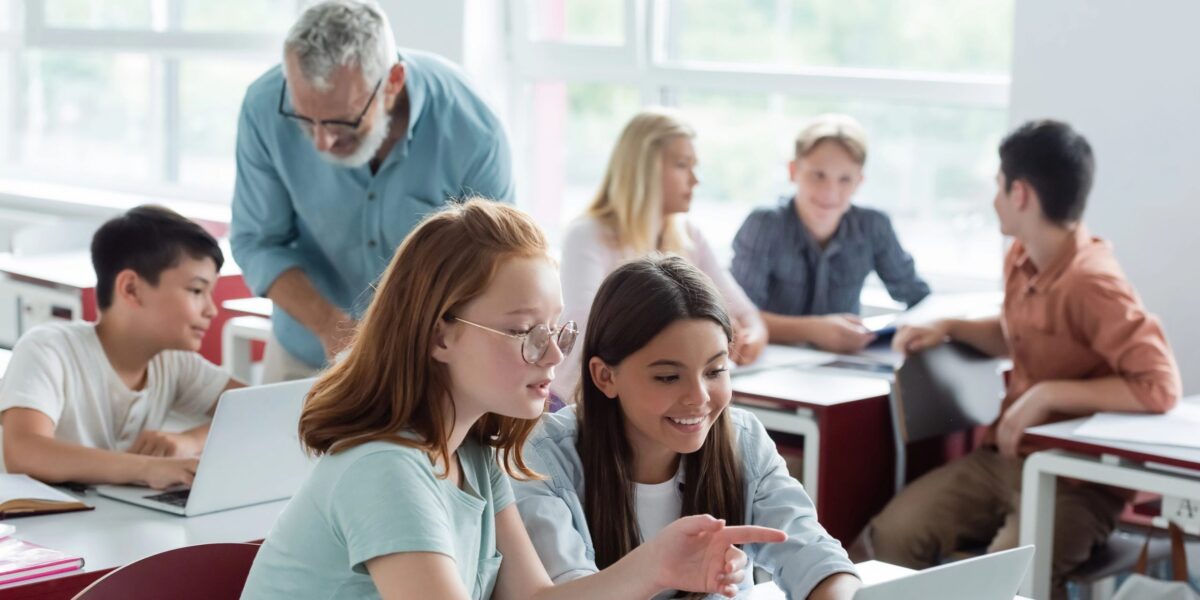 Lehrer in Klasse mit Schülern am Laptop