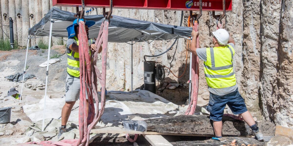 Ein bis zu 250 kg schwerer Eichenbalken wird vorsichtig aus der Baugrube am Aschaffenburger Mainufer gehoben