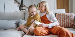 Person sitzt auf einem Bett, am Oberarm ein Glukosesensor, in den Händen ein Smartphone