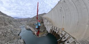 Frau hängt an Seil vor Staumauer
