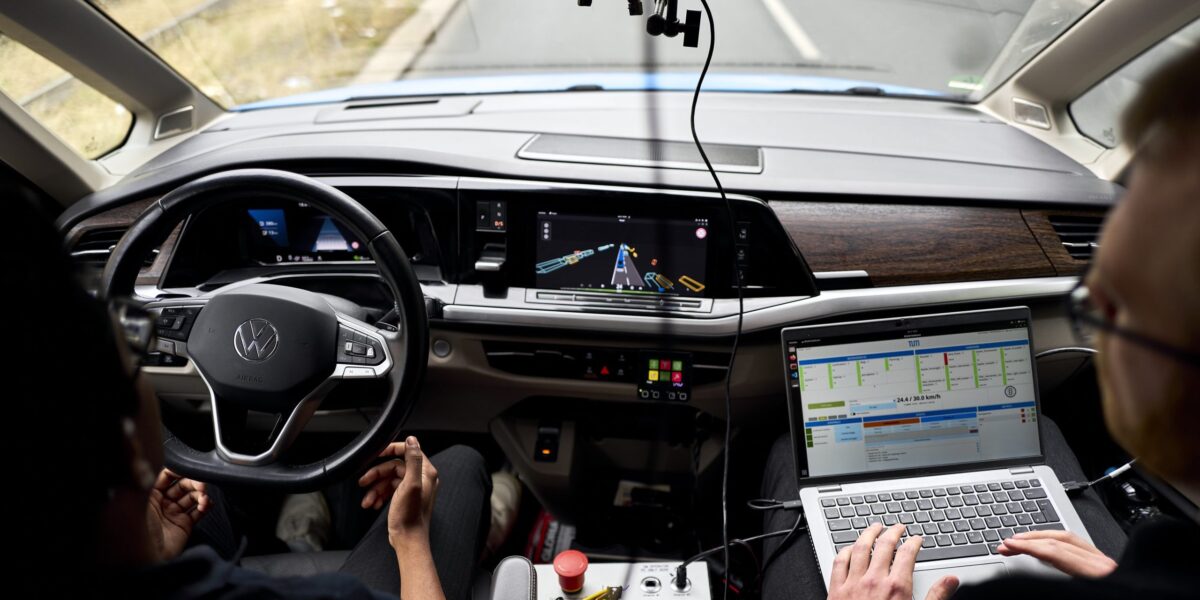 Blick über die Schultern zweier Personen im Cockpit eines VW-Testfahrzeugs auf der Autobahn