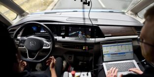 Blick über die Schultern zweier Personen im Cockpit eines VW-Testfahrzeugs auf der Autobahn