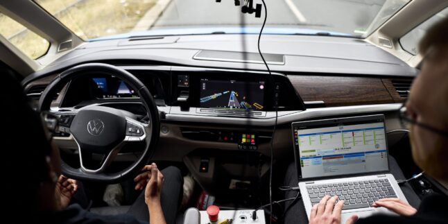 Blick über die Schultern zweier Personen im Cockpit eines VW-Testfahrzeugs auf der Autobahn