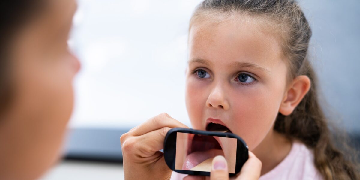 Ärztin hält ein Smartphone vor den geöffneten Mund eines Mädchens