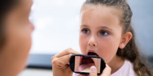 Ärztin hält ein Smartphone vor den geöffneten Mund eines Mädchens