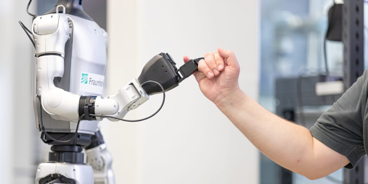 Humanoider Roboter und Mensch reichen sich den kleinen Finger