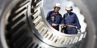 Industriearbeiter durch eine große Zahnradachse gesehen.