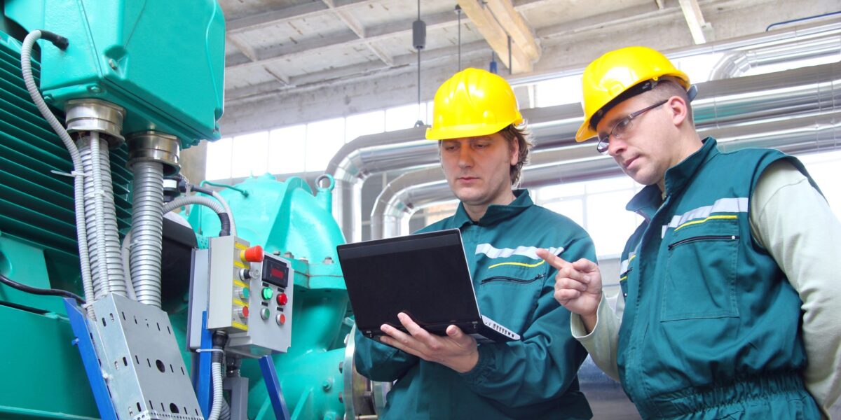 Zwei Ingenieure stehen vor einer Maschine mit einem Laptop in der Hand und testen etwas.