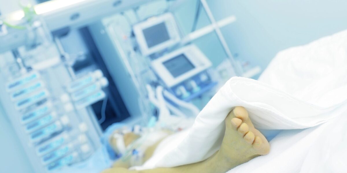 Krankenhaus mit Apperaturen im Hintergrund, auf dem Bett ist ein Fuß zu sehen