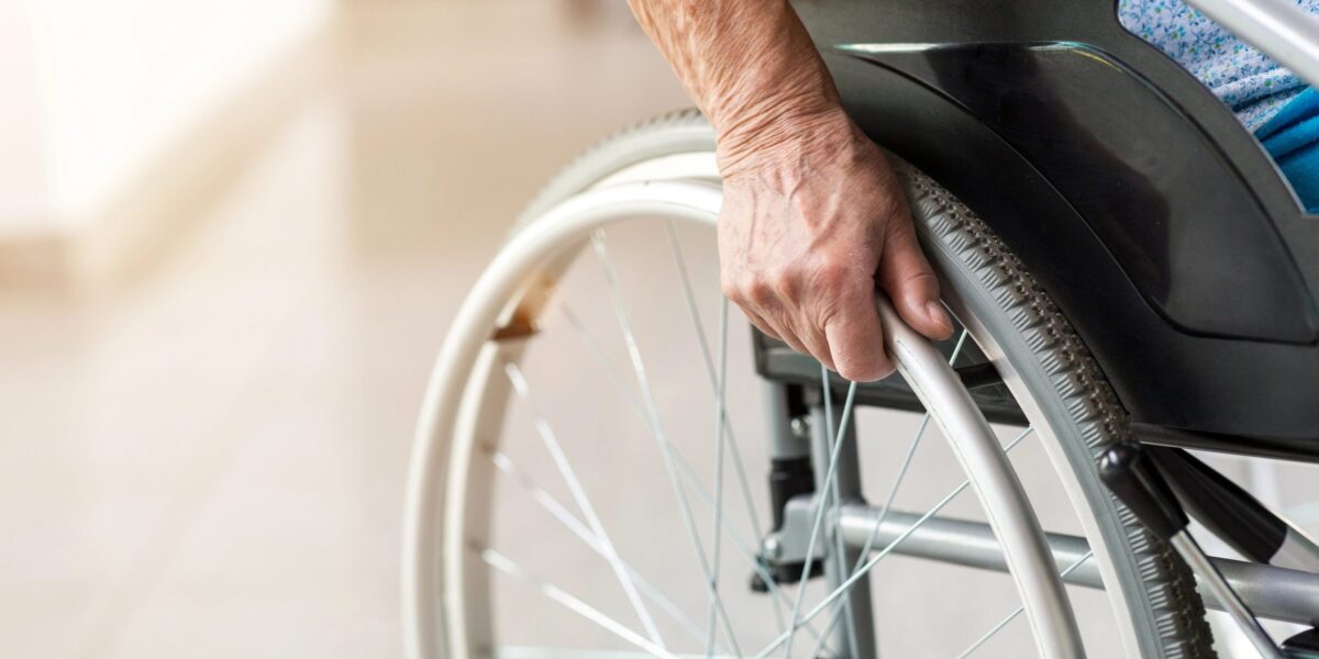 Eine Person sitzt im Rollstuhl, man sie die Hand und das Rad
