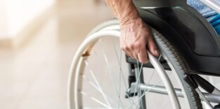 Eine Person sitzt im Rollstuhl, man sie die Hand und das Rad