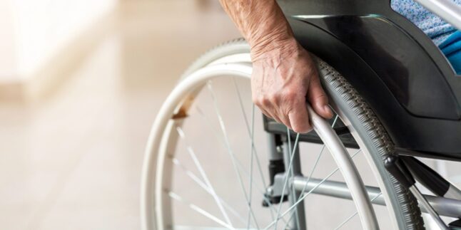 Eine Person sitzt im Rollstuhl, man sie die Hand und das Rad