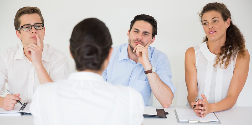 Drei Personen im Business-Kontext sitzen einer Frau gegenüber