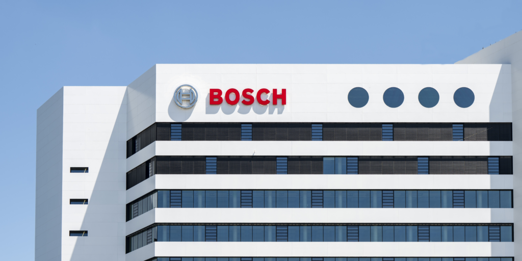 Nahaufnahme eines modernen Bosch-Gebäudes mit weißer Fassade, langen Fensterbändern und rotem Bosch-Schriftzug unter blauem Himmel.