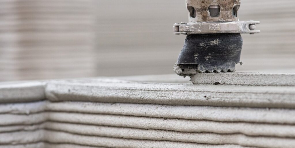 Nahaufnahme einer 3D-Betondruckdüse, die zementgebundenes Material in horizontalen Schichten aufträgt.