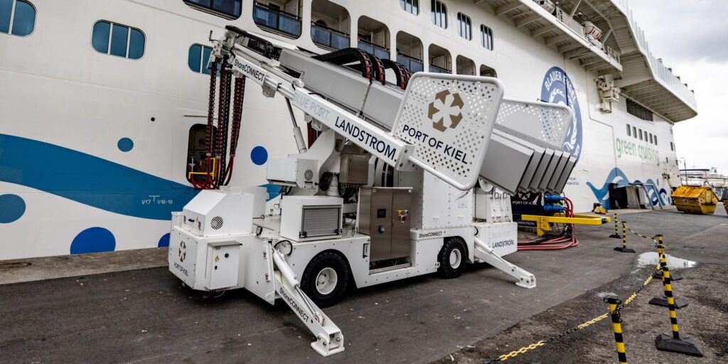 Mobiles Landstromgerät mit der Aufschrift „Landstrom – Port of Kiel" vor einem Kreuzfahrtschiff am Kai