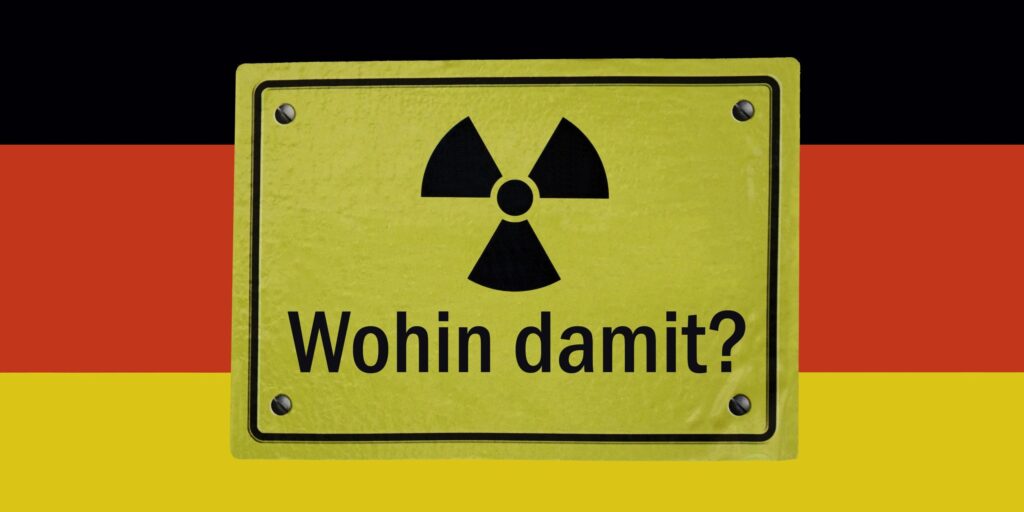 Auf einer Deutschlandfahne befindet sich ein gelbes Schild mit dem Symbol der Radioaktivität und dem schwarzen Schriftzug "Wohin damit?"