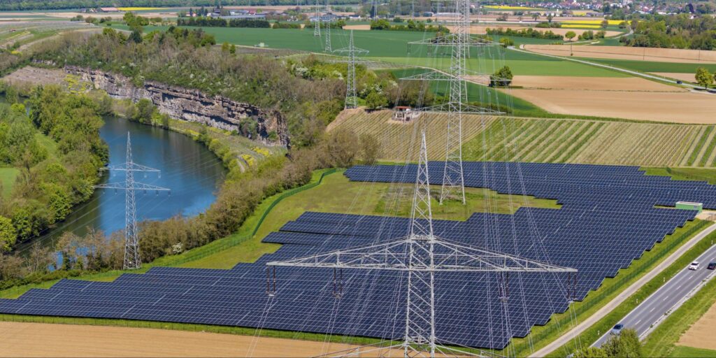 Luftaufnahme Stromtrasse vor Solarpark in Flußaue