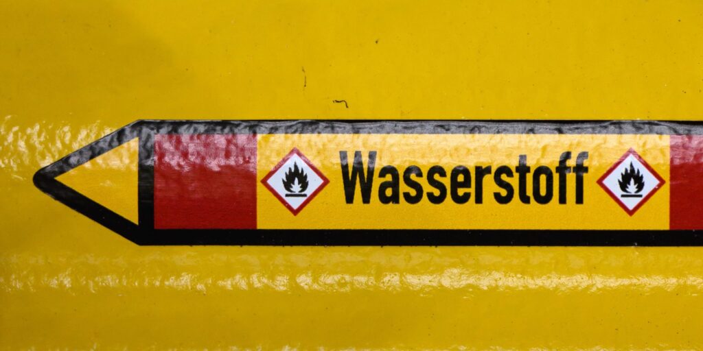 Gelbe Rohrleitung mit Kennzeichnungspfeil und der Aufschrift „Wasserstoff" sowie zwei Gefahrensymbolen für entzündliche Stoffe.