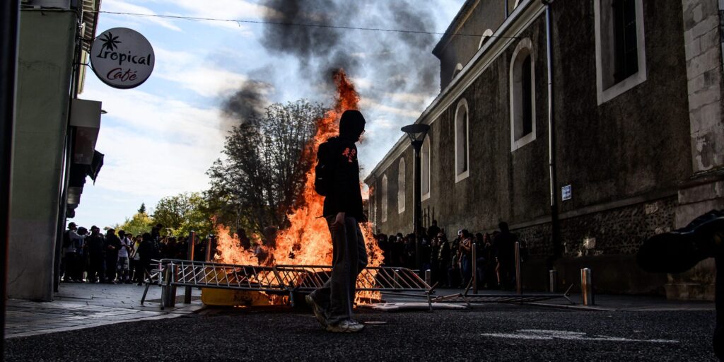 Jugendliche bei einem Protest in Frankreich vor einer brennenden Barrikade auf einer Straße.